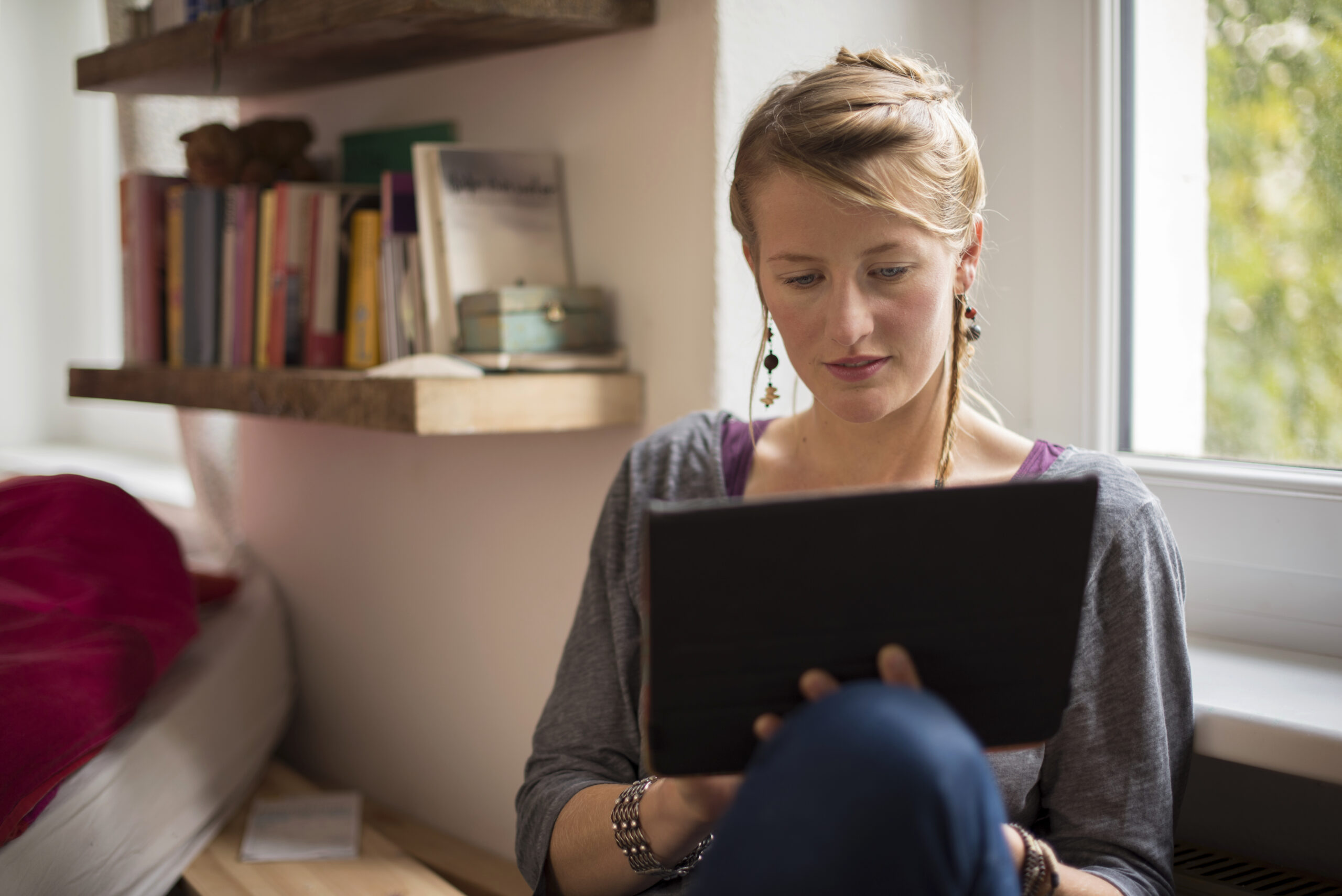 Eine junge Frau sitzt mit Tablet in der Hand auf dem Sofa.