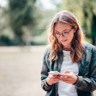 Eine junge Frau steht in einem Park und guckt auf ihr Handy.